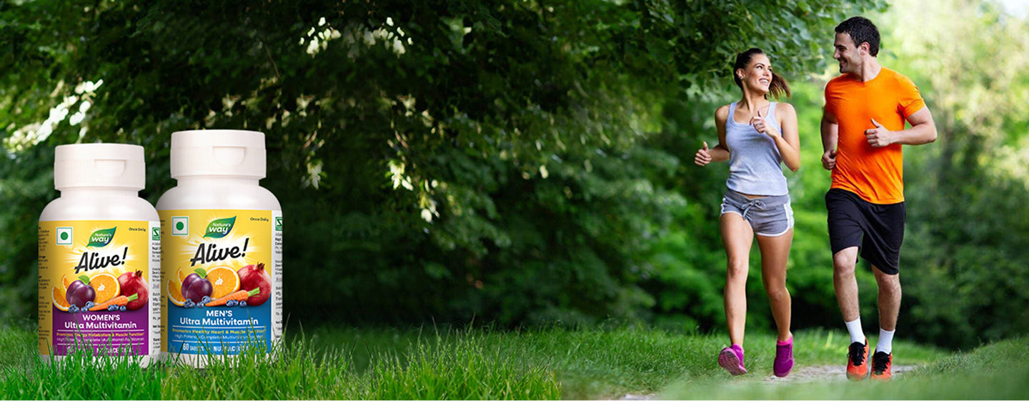 Nature’s Way Alive! Women’s and Men’s Ultra Multivitamin bottles on grass with a smiling couple jogging on a tree-lined trail in the background.